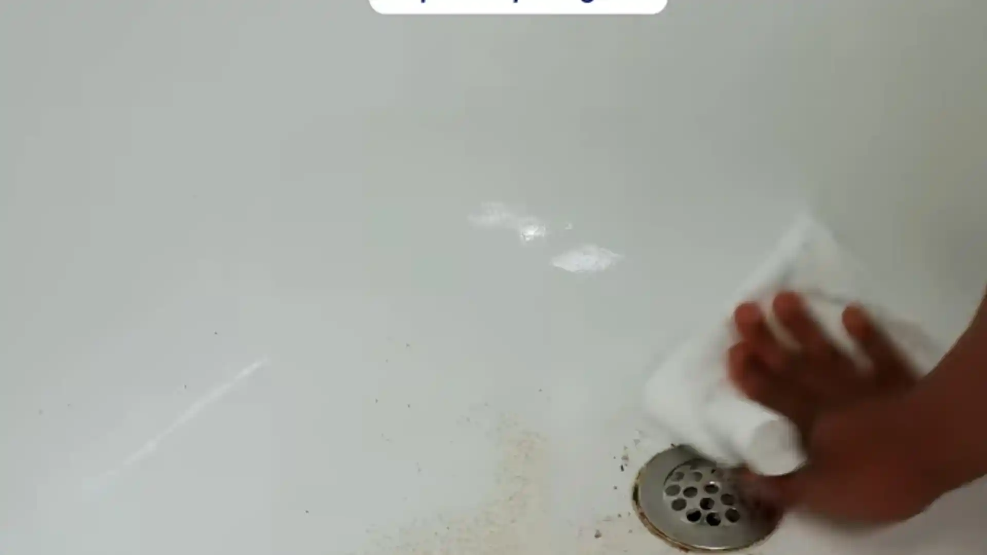 Hands cleaning grime and residue near a bathtub drain