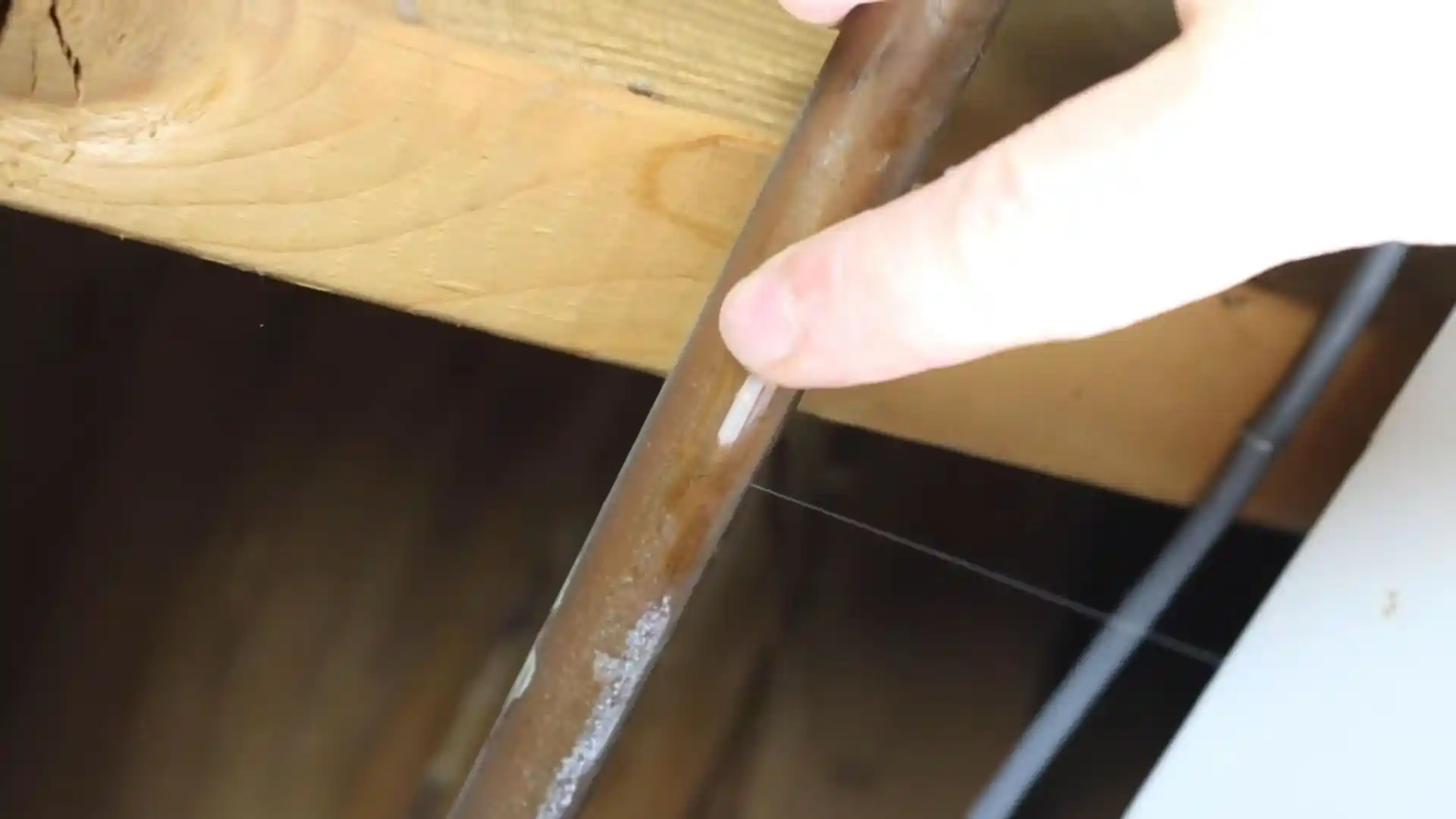 Close-up of a hand inspecting a corroded pipe with a visible leak point