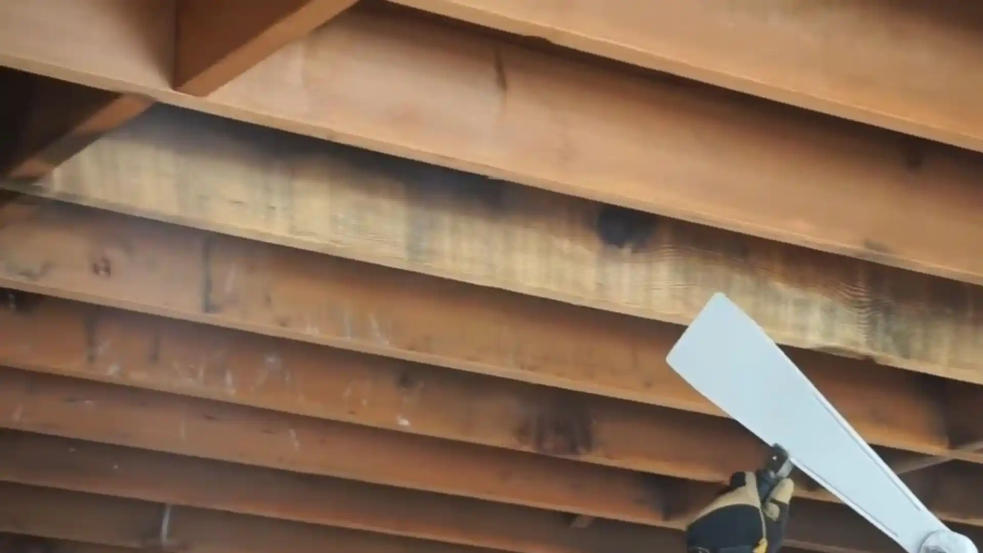 Technician scraping soot from charred wood ceiling joists after a house fire
