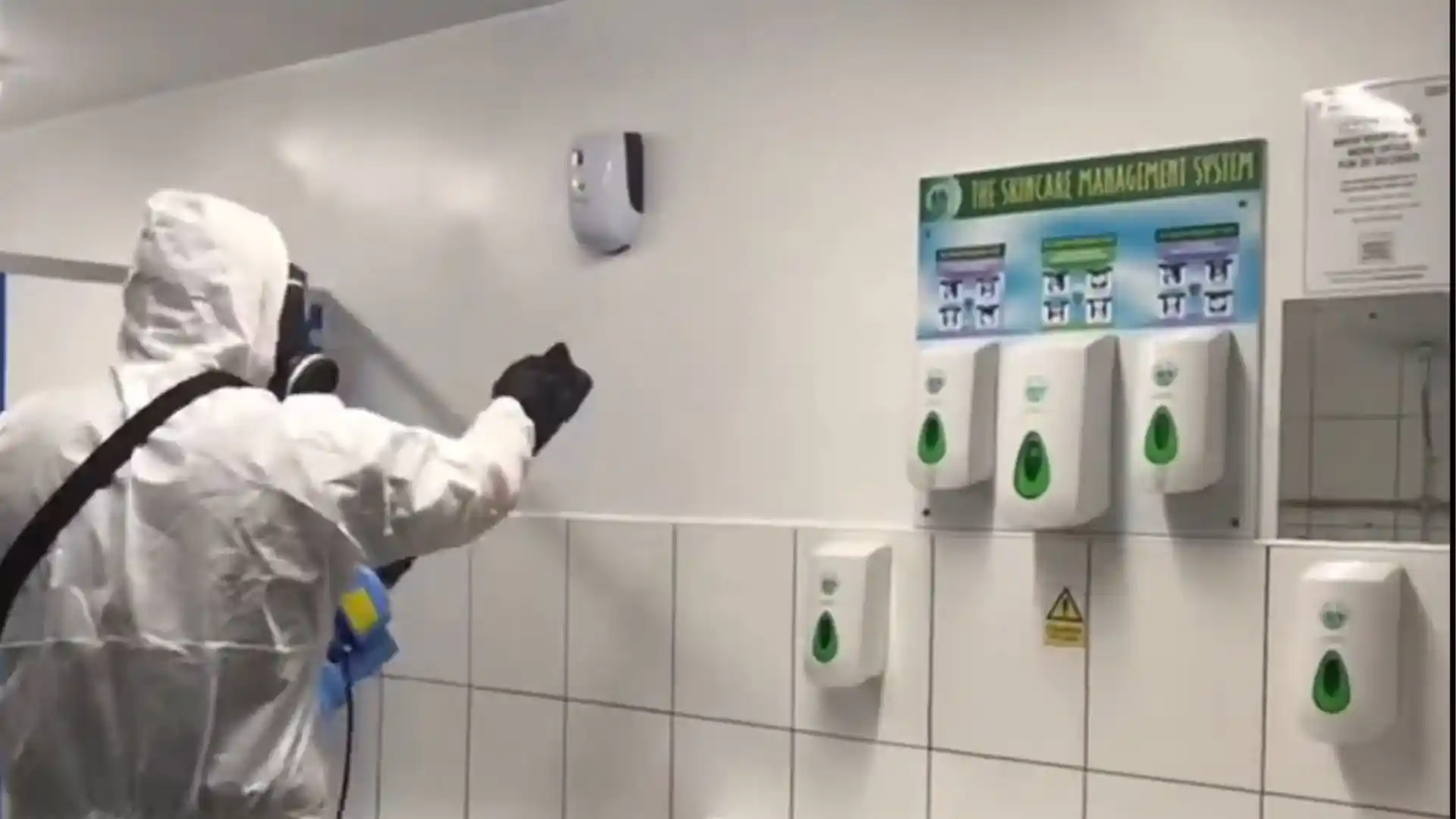 Technician in protective coveralls disinfecting a wall in a commercial restroom