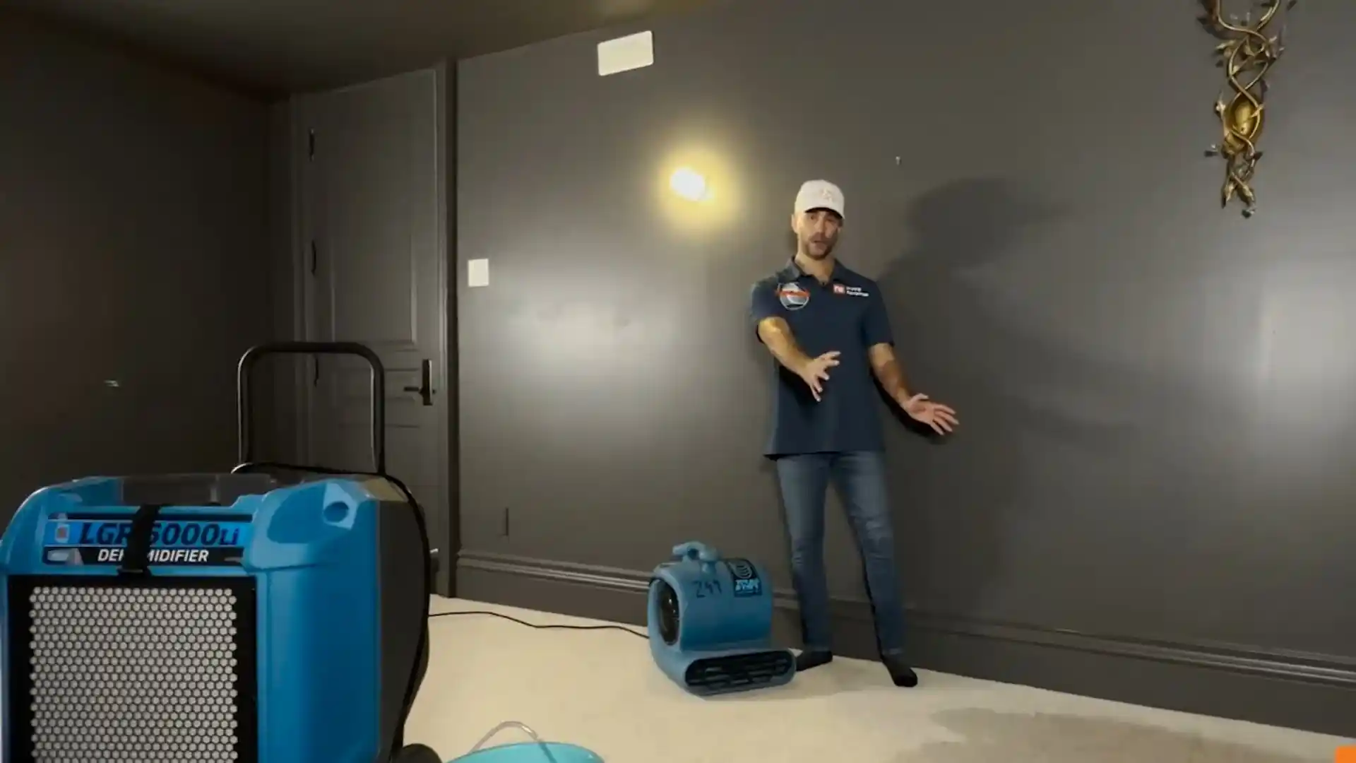 Restoration technician standing beside a dehumidifier and air mover set up to dry a room