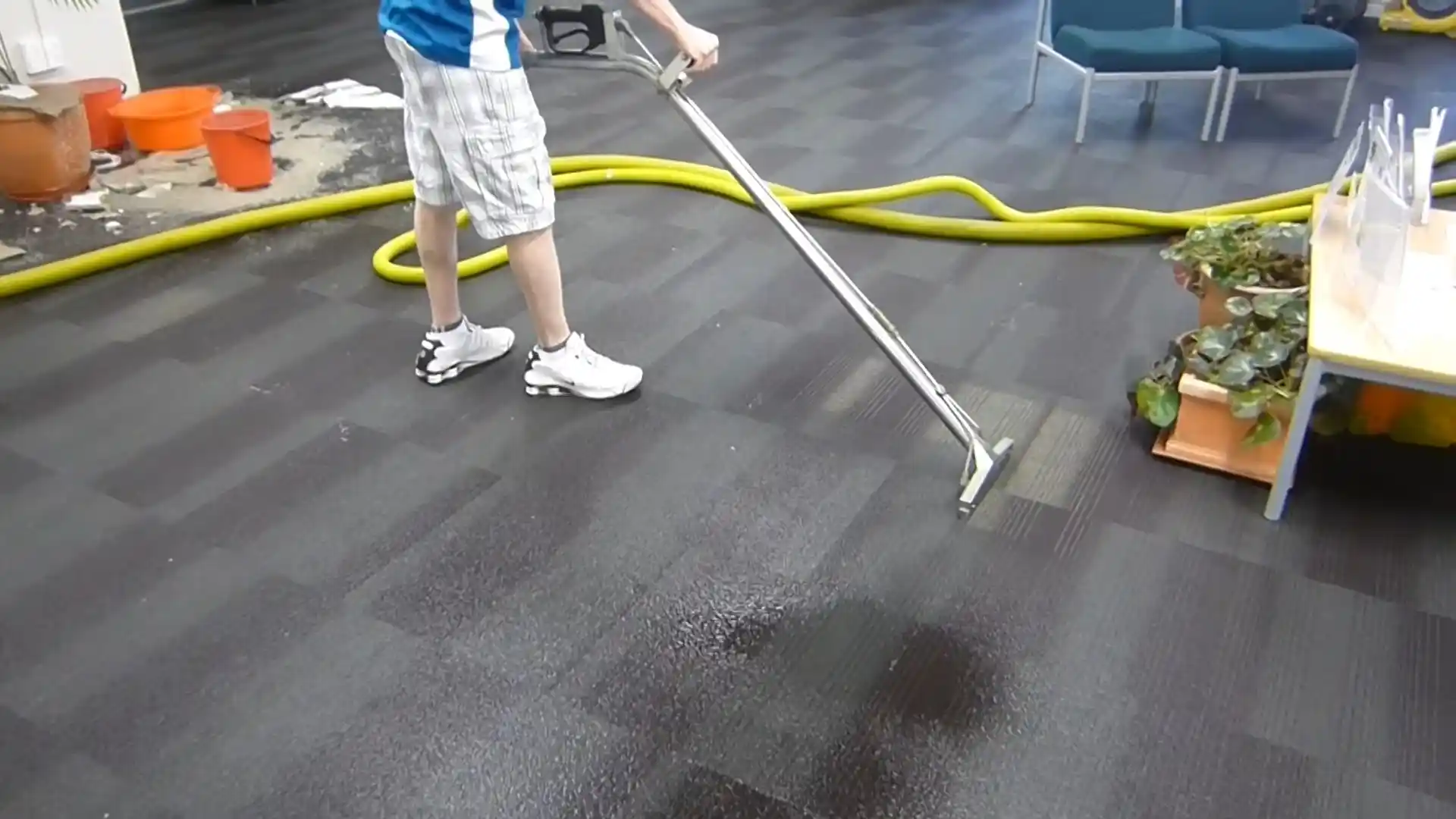 Technician using a truck-mount extraction wand on wet commercial carpet tile