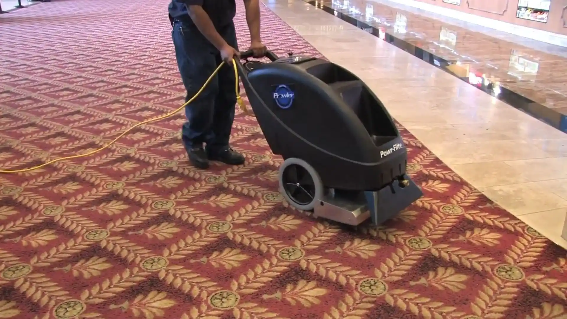 Technician operating a walk-behind carpet extractor in a hotel or commercial hallway